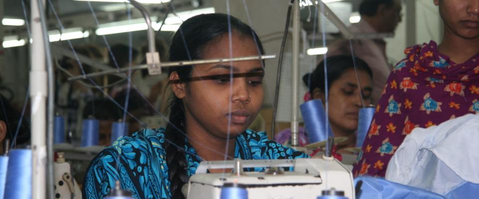 Des ouvriers du textile cousant sur des machines industrielles dans une usine textile en pleine activité.
