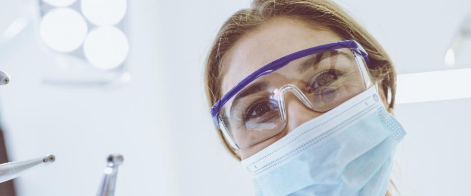 Smiling person wearing surgical mask and holding dental tool