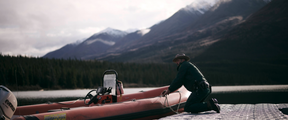 Un employé de Parcs Canada travaille sur un bateau en plein air dans le Yukon, avec des montagnes en arrière-plan.