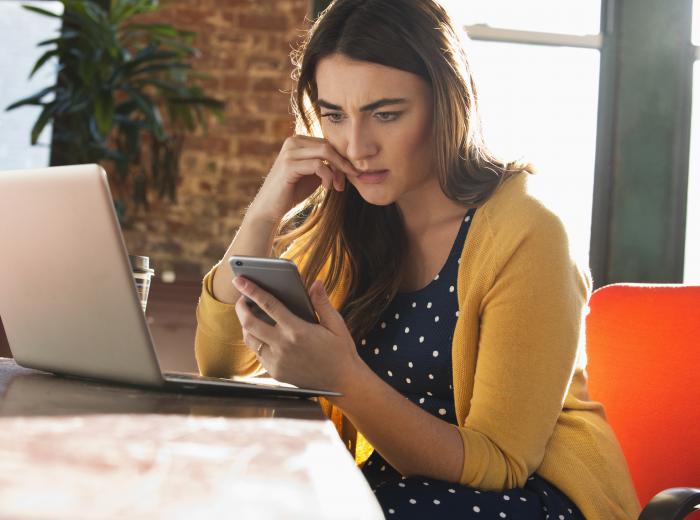Une femme regarde son téléphone avec une expression inquiète.