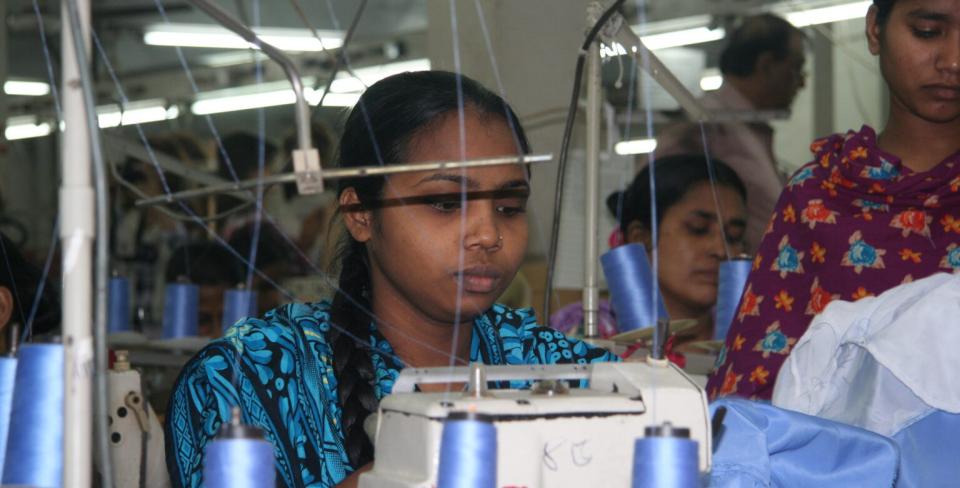 Des ouvriers du textile cousant sur des machines industrielles dans une usine textile en pleine activité.
