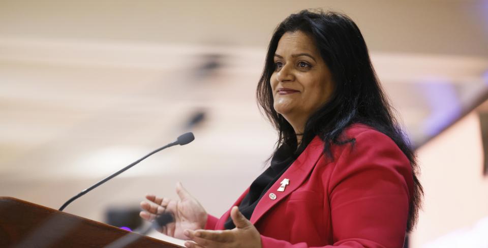 Sharon DeSousa sourit et parle à un microphone. 