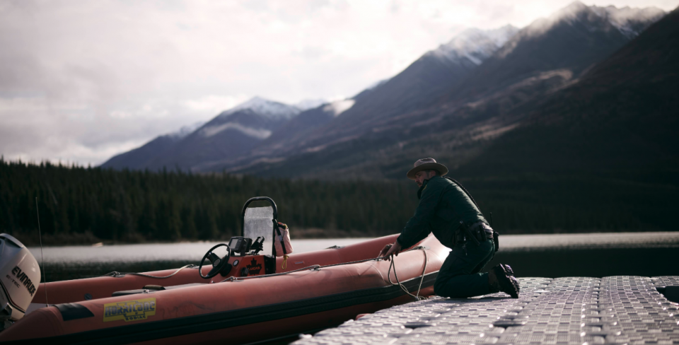 Un employé de Parcs Canada travaille sur un bateau en plein air dans le Yukon, avec des montagnes en arrière-plan.